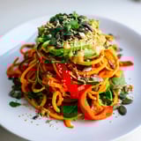 The colorful Carrot Noodle Skincare Bowl features spiralized carrots, fresh greens, and a drizzle of creamy tahini dressing.  