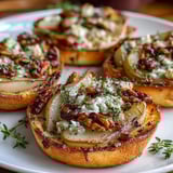 A close-up of rustic pear, Gorgonzola, and pickled walnut pizzettes, drizzled with honey and served on a wooden board.