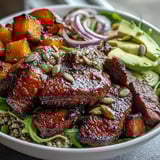 Fork-tender butternut squash steak bowls are topped with vibrant greens, red onion, and crunchy toasted pepitas.