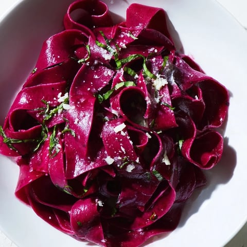Freshly cut beet noodle pasta in a vibrant magenta hue, ready to be cooked and tossed with herbs.