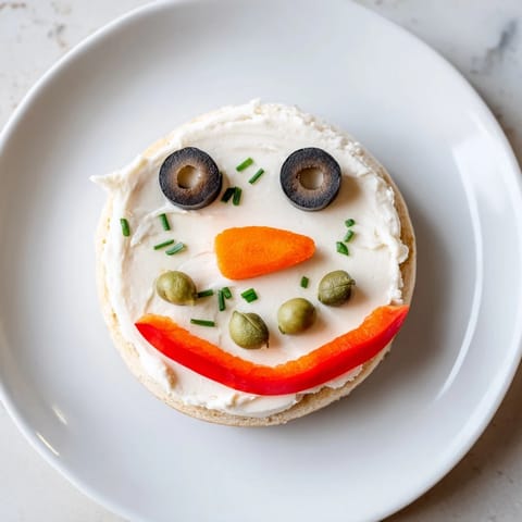 Adorable Snowman Mini Bagel Sandwiches, adorned with olive eyes and carrot noses, perfect for kids.