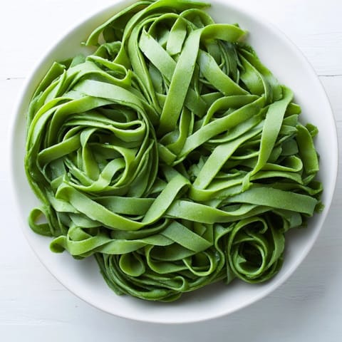 Homemade spinach pasta dough wrapped in plastic, resting before being rolled into sheets.