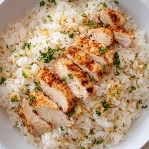 Golden garlic butter rice and tender grilled chicken breast served in a white ceramic bowl for a comforting meal.