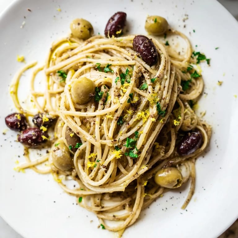 Savory olive tapenade pasta served in a white bowl, garnished with fresh parsley and lemon zest for a bright Mediterranean flavor.