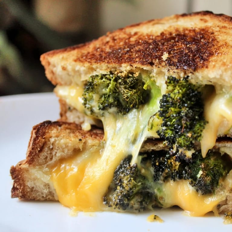 Close-up of a crispy grilled cheese sandwich revealing oozing sharp cheddar and tender roasted broccoli pieces.